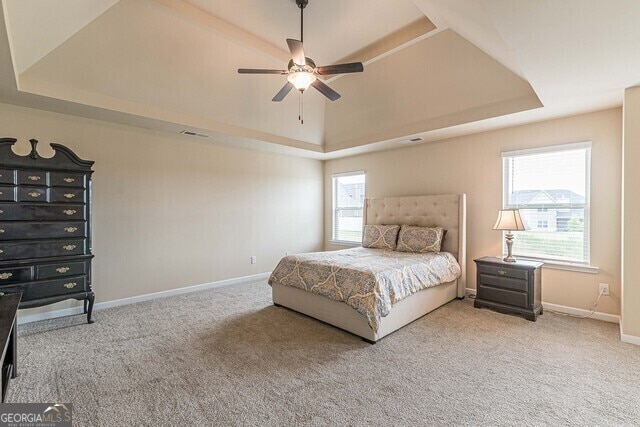 bedroom featuring ceiling fan, light colored carpet, and a tray ceiling