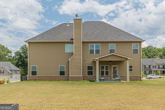 rear view of house with central AC unit, ceiling fan, a patio area, and a lawn