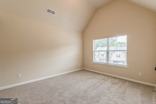 carpeted empty room featuring vaulted ceiling