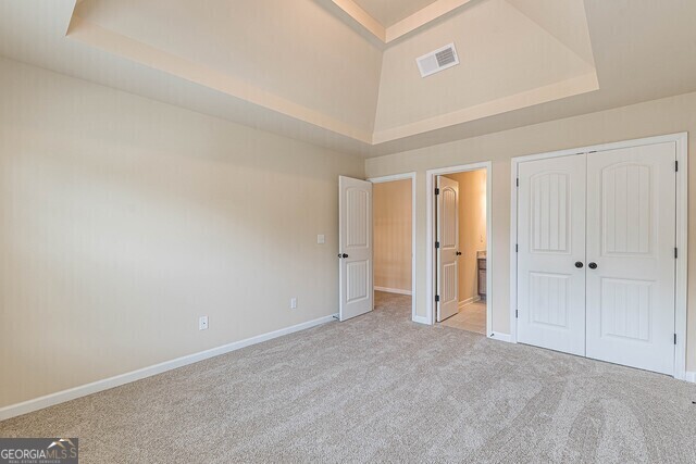 unfurnished bedroom with a tray ceiling, connected bathroom, light carpet, and a closet