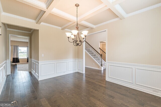 empty room featuring dark hardwood / wood-style flooring, ornamental molding, coffered ceiling, a notable chandelier, and beamed ceiling