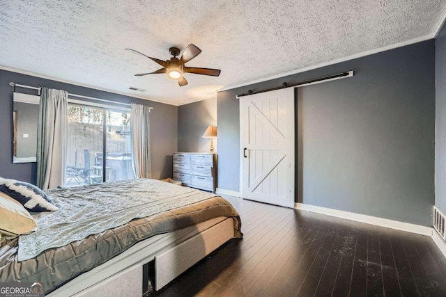 bedroom featuring dark hardwood / wood-style flooring, a textured ceiling, ceiling fan, crown molding, and a barn door