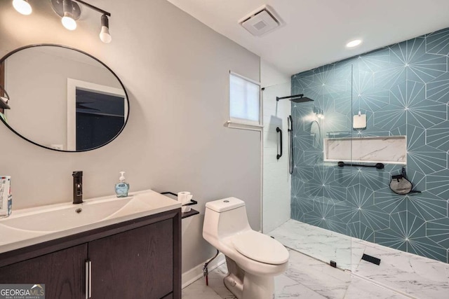 bathroom with a tile shower, vanity, and toilet