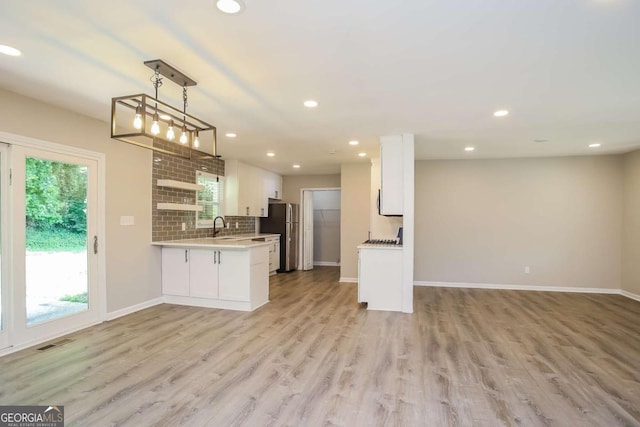 kitchen featuring kitchen peninsula, light hardwood / wood-style flooring, white cabinetry, hanging light fixtures, and stainless steel refrigerator