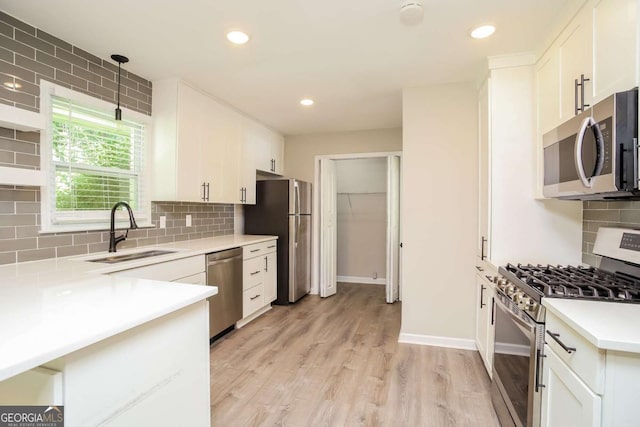 kitchen featuring sink, light hardwood / wood-style floors, pendant lighting, white cabinets, and appliances with stainless steel finishes