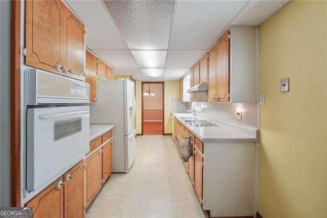 kitchen with white appliances, a drop ceiling, and sink