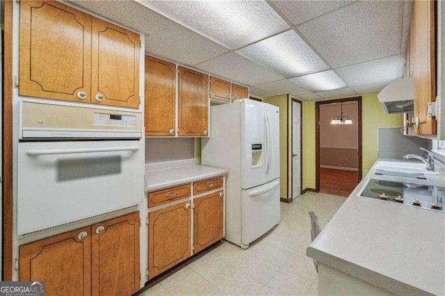 kitchen featuring a paneled ceiling, white appliances, exhaust hood, sink, and a notable chandelier