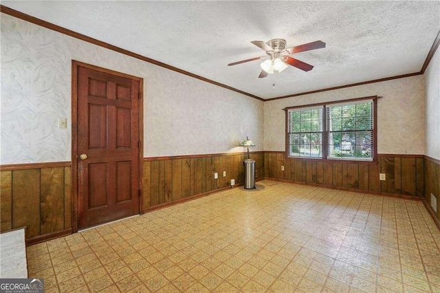 unfurnished room with a textured ceiling, crown molding, ceiling fan, and wooden walls