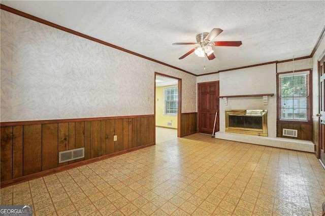 unfurnished living room featuring wooden walls, ceiling fan, a textured ceiling, and ornamental molding