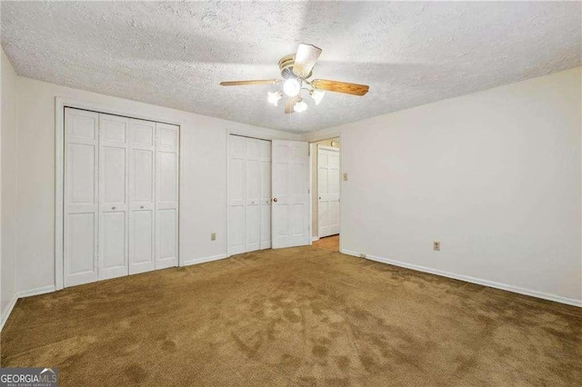 unfurnished bedroom with carpet flooring, multiple closets, ceiling fan, and a textured ceiling