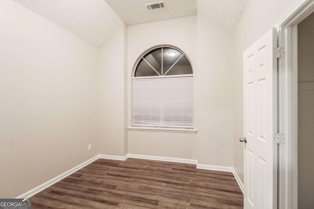 empty room with a textured ceiling, lofted ceiling, and dark wood-type flooring