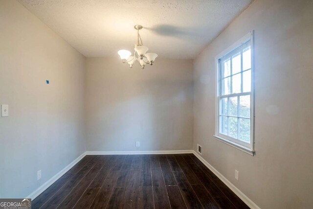 empty room featuring dark wood-type flooring, a textured ceiling, and an inviting chandelier