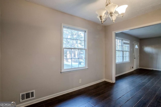 spare room featuring dark wood-type flooring and an inviting chandelier