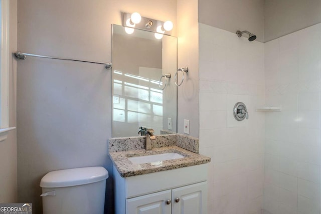 bathroom featuring a tile shower, vanity, and toilet