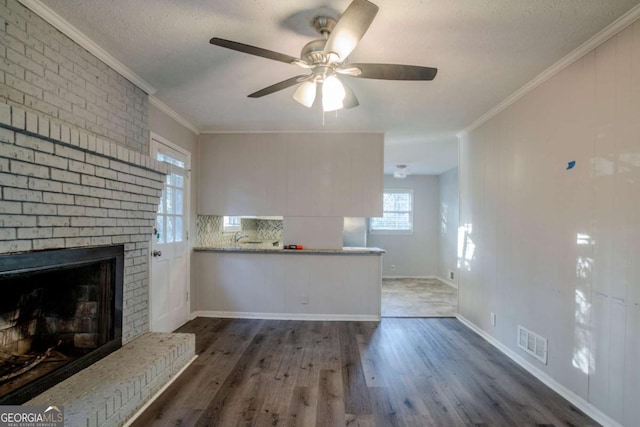 unfurnished living room featuring ornamental molding, a textured ceiling, ceiling fan, a fireplace, and dark hardwood / wood-style floors