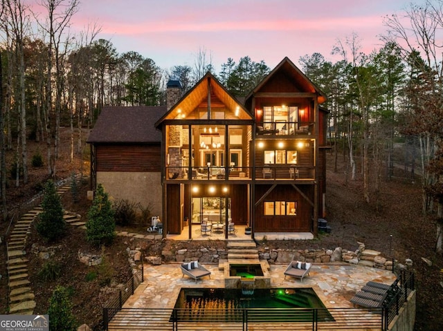 back house at dusk with a balcony and a patio