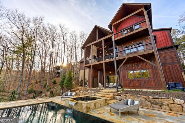 rear view of property featuring a pool with hot tub, a patio area, and a balcony