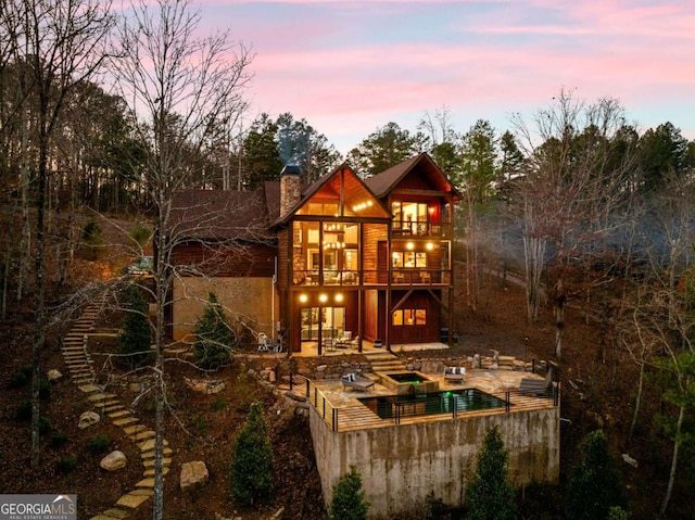 back house at dusk featuring a swimming pool with hot tub, a balcony, and a patio