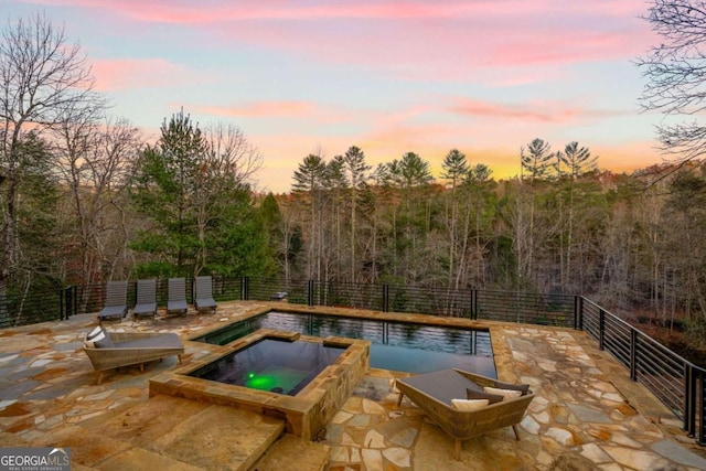 pool at dusk with an in ground hot tub and a patio