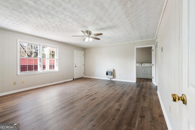 spare room with heating unit, ceiling fan, washing machine and dryer, dark hardwood / wood-style floors, and wood walls