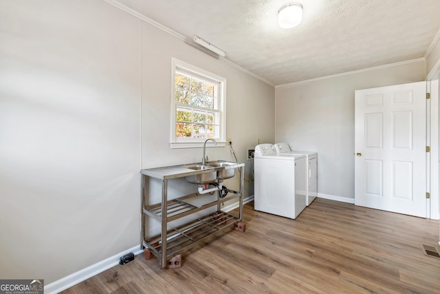 clothes washing area with hardwood / wood-style flooring, washer and clothes dryer, ornamental molding, and sink