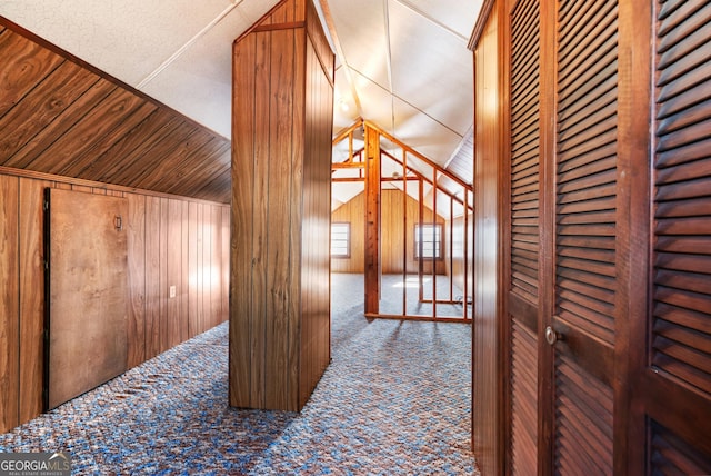 corridor with carpet flooring, wooden walls, and lofted ceiling