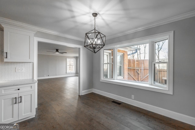 unfurnished dining area with dark wood-type flooring, ceiling fan with notable chandelier, and ornamental molding