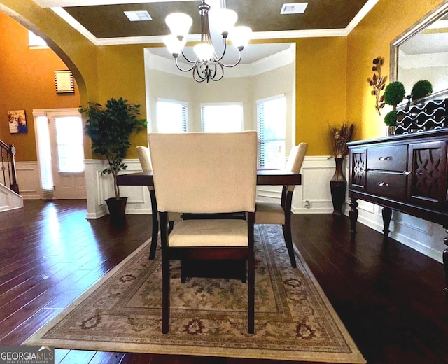 dining room with arched walkways, wainscoting, crown molding, and an inviting chandelier