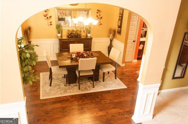 dining space with a wainscoted wall, wood finished floors, arched walkways, an inviting chandelier, and a decorative wall