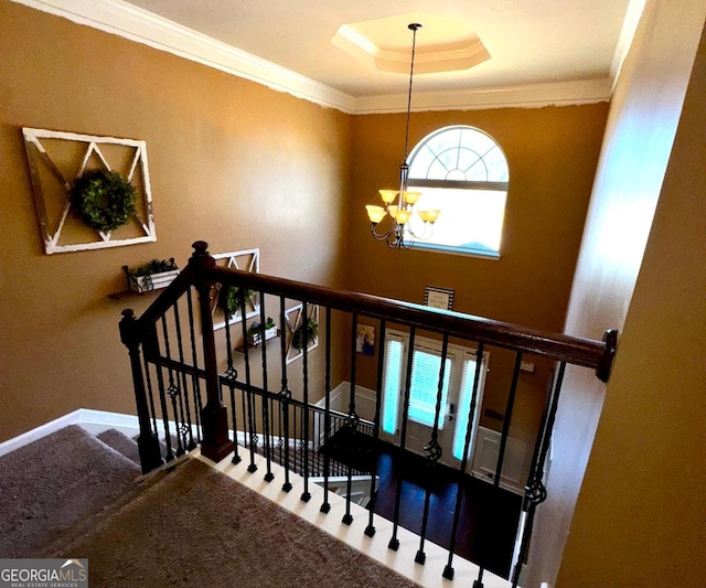 stairs featuring baseboards, ornamental molding, carpet flooring, an inviting chandelier, and a raised ceiling