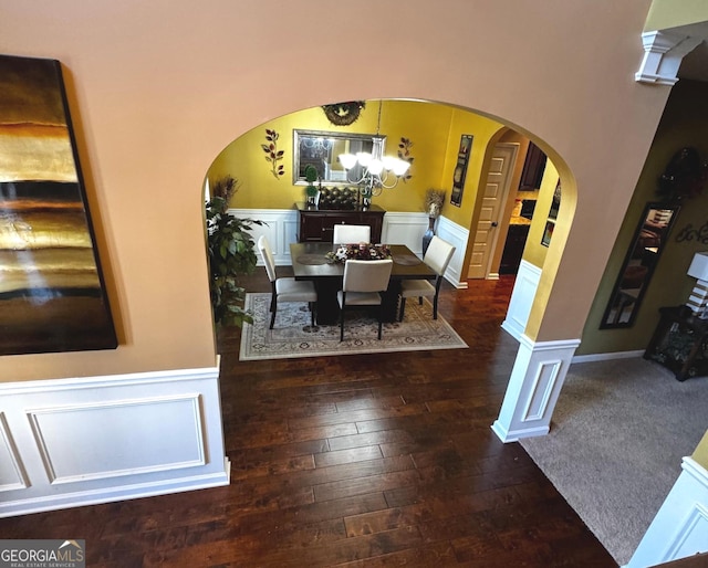 dining space with arched walkways, an inviting chandelier, hardwood / wood-style floors, and wainscoting