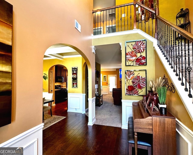 entrance foyer with dark wood-type flooring, a wainscoted wall, ornamental molding, arched walkways, and a decorative wall