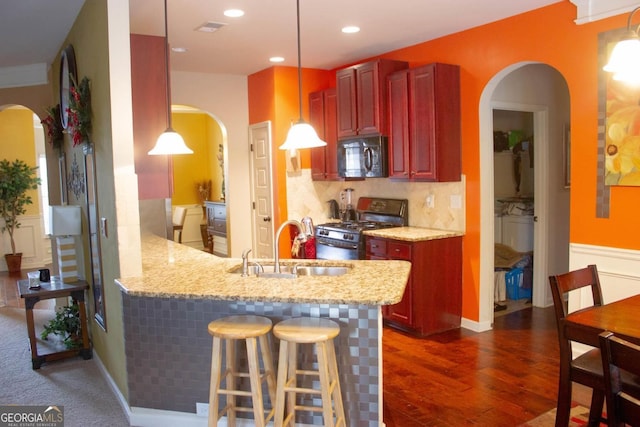 kitchen with a sink, gas stove, arched walkways, reddish brown cabinets, and black microwave