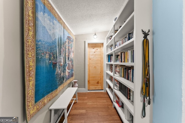 hall featuring vaulted ceiling, light hardwood / wood-style floors, and a textured ceiling