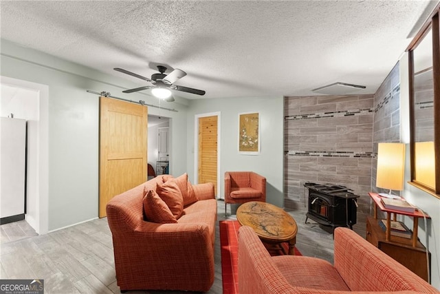 living room with a wood stove, ceiling fan, a textured ceiling, and light wood-type flooring