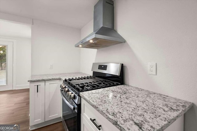 kitchen featuring wall chimney exhaust hood, stainless steel gas range oven, light stone counters, and white cabinetry