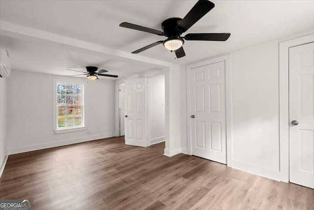 unfurnished bedroom with a wall mounted AC, wood-type flooring, and ceiling fan