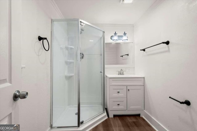 bathroom with vanity, wood-type flooring, a shower with shower door, and ornamental molding