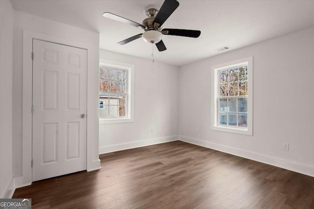 unfurnished bedroom featuring multiple windows, ceiling fan, and dark wood-type flooring