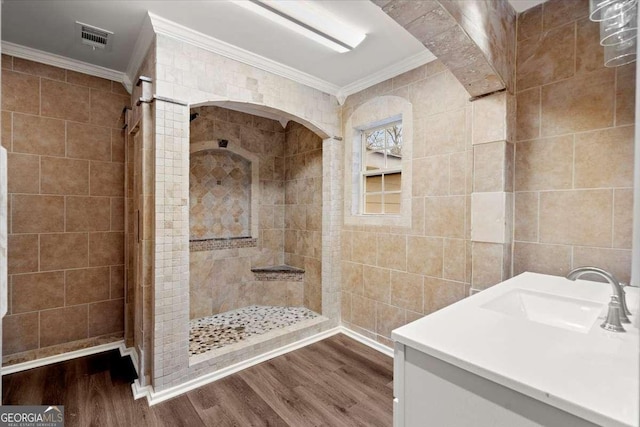 bathroom featuring a tile shower, wood-type flooring, tile walls, and ornamental molding