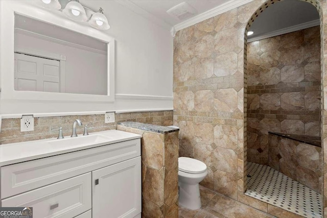 bathroom featuring vanity, toilet, ornamental molding, tiled shower, and tile walls