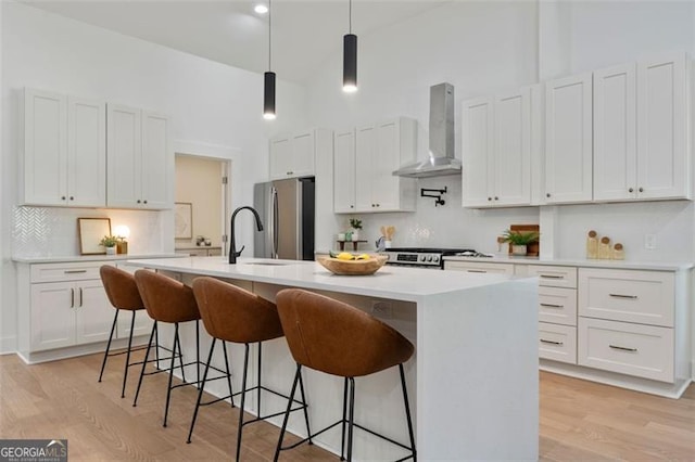 kitchen featuring white cabinets, wall chimney range hood, appliances with stainless steel finishes, and light countertops