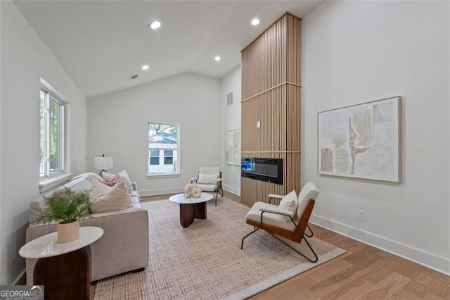 living area with vaulted ceiling, a fireplace, plenty of natural light, and light wood-style flooring