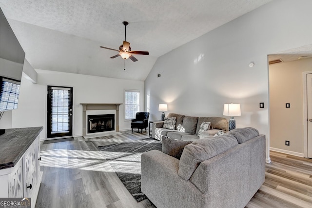 living room featuring ceiling fan, light hardwood / wood-style floors, a textured ceiling, and high vaulted ceiling