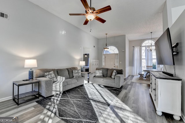 living room with ceiling fan with notable chandelier, wood-type flooring, a textured ceiling, and high vaulted ceiling