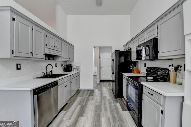 kitchen with decorative backsplash, sink, black appliances, light hardwood / wood-style flooring, and gray cabinets