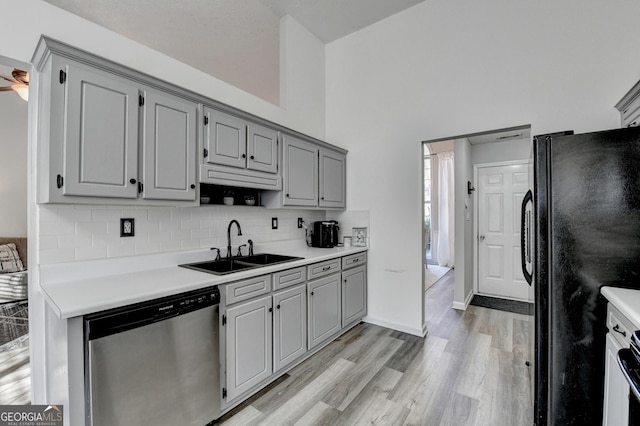 kitchen featuring dishwasher, sink, backsplash, black refrigerator, and light wood-type flooring