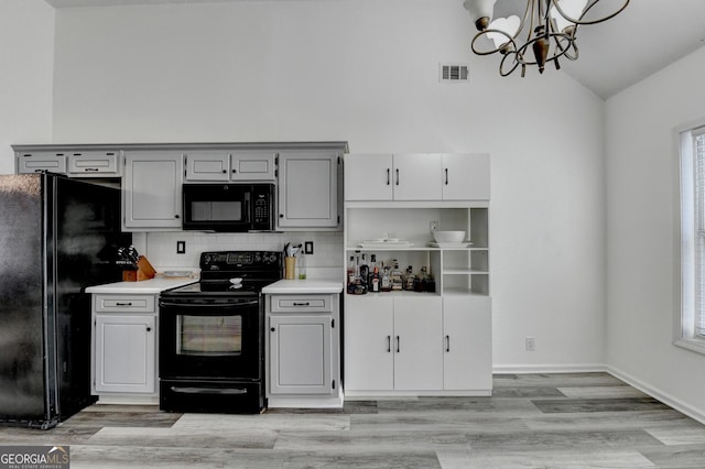 kitchen with pendant lighting, black appliances, vaulted ceiling, and light wood-type flooring