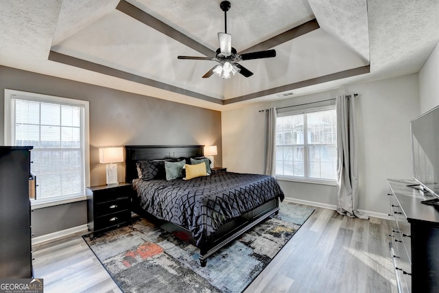 bedroom featuring a textured ceiling, light wood-type flooring, a tray ceiling, and ceiling fan