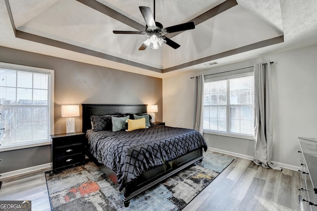 bedroom featuring a raised ceiling, multiple windows, and ceiling fan